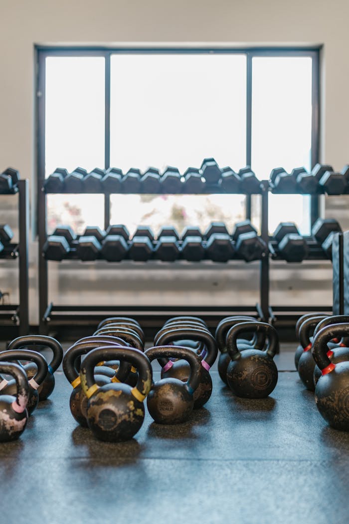 services-01 A well-lit gym with kettlebells and dumbbells arranged neatly, ideal for workout inspiration.
